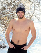 Serious handsome young man or sexy muscular gay with bare torso and naked chest body in winter hat outdoor in trees with snow