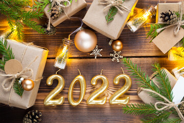 Figures candles 2022 on a wooden background with fairy lights, gifts box and eco-friendly Christmas decor. Tags with mock up, natural decor, cones, needles. Festive mood. Flatly, new year background