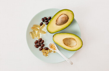 Health care and diet concept. Avocado and fish oil in capsules for vitamin D and omega-3 fatty acids in a plate on a white background