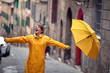 A young girl with a yellow raincoat and umbrella is enjoying a rainy weather on the street. Walk, rain, city