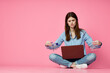 © VICHIZH - woman sitting on floor with laptop shopping entertainment pink background
