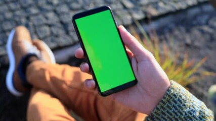Young man hand holding smartphone with blank green screen. Sunset sunlight rising on background. Businessman freelance lifestyle. Chroma key display. Traveling app online. Network communication. 