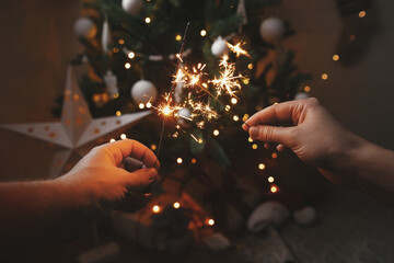 Happy New Year! Couple hands holding burning sparklers on background of christmas tree lights