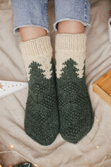 Wall Mural - Woman feet in woolen socks on soft bed with warm cup of tea, christmas stars, golden lights