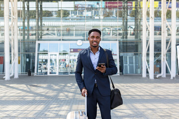 Wall Mural - successful young confident African American businessman moving with cellphone in hands against modern office building background downtown black business man walks using a mobile phone in formal suit