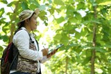 Fototapeta  - Asian female backpack hiker travel alone in forest , take photos, survey and collect information of botanical plants by using smart tablet. Concept :  backpacking tourism, adventure, field research 