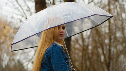 young girl with umbrella walking in at beautifu autumn park. modern girl in casual clothes walks through the city park. Seasonal style, autumn beauty. autumn season, in a blue jacket, in autumn leaves