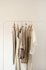Wall Mural - Minimal aesthetic fashion clothes concept. Neutral beige washed linen female blouses, dresses and t-shirts on hanger on white background. Fashion blog, website, social media
