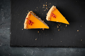 Canvas Print - Flat lay of cheesecake with yellow mango flavoured layer decorated with red crumbs of freeze-dried raspberries. Cake cut on the dark marble background