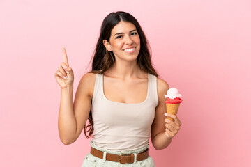 Young caucasian woman with a cornet ice cream isolated on pink background showing and lifting a finger in sign of the best