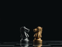 The Confront Between Golden And Silver Horses, Knight Chess Piece Standing Together On Chessboard On Dark Background. Leadership, Partnership, Competitor, Competition, And Business Strategy Concept.