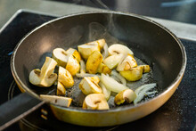 Cut Champignon Mushrooms With Onions On A Sizzling Frying Pan. Thin Smoke Over The Hot Frying Pan Close Up.