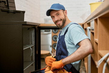 Canvas Print - Joyful bearded man repairing fridge in cafe