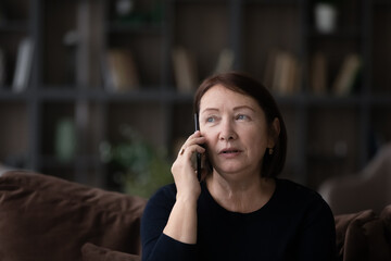 head shot close up of serious mature woman talking on phone at home sitting on couch, senior female 