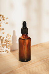 Wall Mural - Amber dropper bottle with serum or essential oil on natural wooden background with daylight. Skincare products , natural cosmetic with with dry plants. Beauty concept for face body care