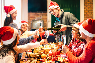 Wall Mural - Millenial friends on santa hats celebrating Christmas with champagne and sweets food at log cabin - Winter holidays concept with young people enjoying time and having fun eating together - Warm filter