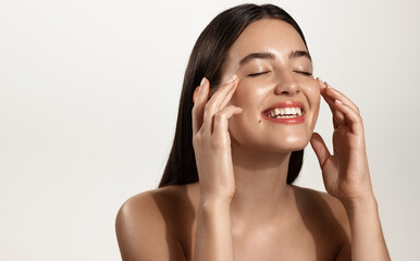 Smiling woman with clean glowing facial skin washing her face, rubbing in cream skincare product for anti-aging, lifting spa effect, standing over white background