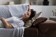 © fizkes - Smiling relaxed woman lying on comfortable couch at home alone, happy beautiful young female resting on soft pillows, taking day nap or daydreaming, visualizing good future, enjoying lazy weekend