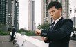 © krumanop - Busy Asian businessman checking time while conection with special customer on bridge near cityscape. Leader manager.