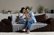 © fizkes - Happy young couple having fun with smartphone at home, sitting on cozy couch, smiling beautiful woman and man in glasses looking at phone screen, watching funny video, surfing internet, chatting
