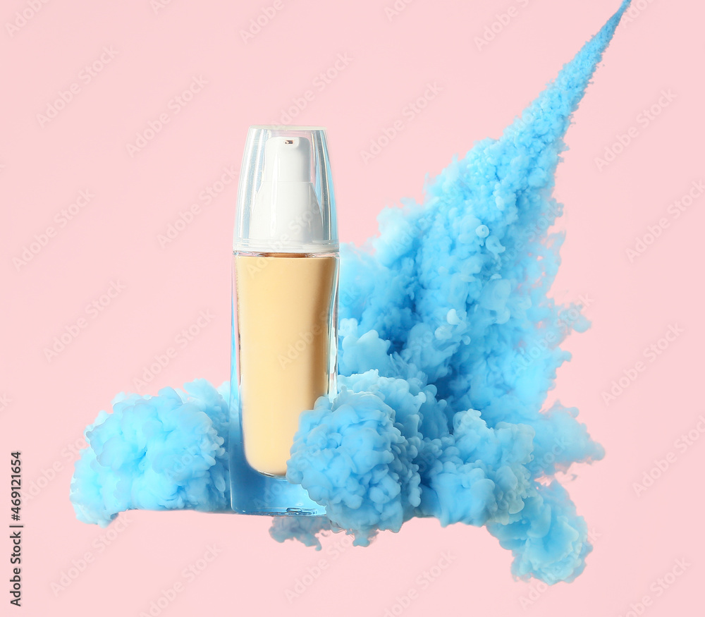 Bottle of makeup foundation in blue smoke on pink background