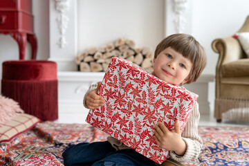 Happy child with gift at home near christmas tree and fireplace