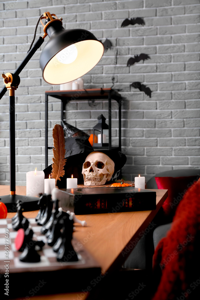 Human skull with witch's hat and candles on table in room decorated for Halloween