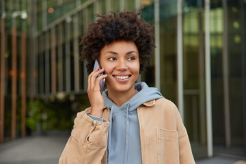 Wall Mural - modern technologies and people concept. happy young curly haired woman enjoys cellular communication