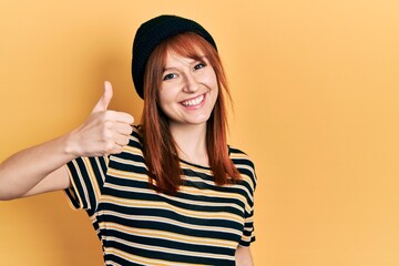 Canvas Print - Redhead young woman wearing wool cap smiling happy and positive, thumb up doing excellent and approval sign