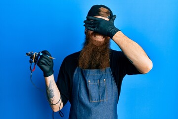 Sticker - Redhead man with long beard tattoo artist wearing professional uniform and gloves smiling and laughing with hand on face covering eyes for surprise. blind concept.