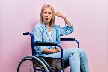 Poster - Beautiful blonde woman sitting on wheelchair angry and mad raising fist frustrated and furious while shouting with anger. rage and aggressive concept.