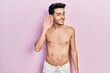 © Krakenimages.com - Young hispanic man wearing swimwear shirtless smiling with hand over ear listening an hearing to rumor or gossip. deafness concept.