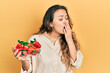 © Krakenimages.com - Young hispanic girl holding strawberries bored yawning tired covering mouth with hand. restless and sleepiness.
