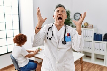 Poster - Middle age doctor man at the clinic with a patient crazy and mad shouting and yelling with aggressive expression and arms raised. frustration concept.