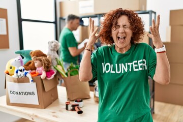 Sticker - Middle age woman wearing volunteer t shirt at donations stand celebrating mad and crazy for success with arms raised and closed eyes screaming excited. winner concept