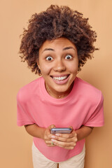 Wall Mural - smiling surprised young woman stares with eyes full of joy uses mobile phone for keeping in touch dr