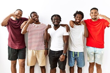 Sticker - Young african group of friends standing together over isolated background smiling doing phone gesture with hand and fingers like talking on the telephone. communicating concepts.