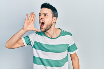 Poster - Young hispanic man wearing casual clothes shouting and screaming loud to side with hand on mouth. communication concept.