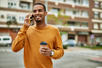 Wall Mural - Young african american man talking on the smartphone drinking coffee at the city.