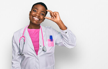 Wall Mural - Young african american woman wearing doctor uniform and stethoscope smiling and confident gesturing with hand doing small size sign with fingers looking and the camera. measure concept.