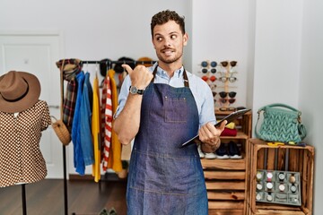 Sticker - Handsome young man working as manager at retail boutique smiling with happy face looking and pointing to the side with thumb up.