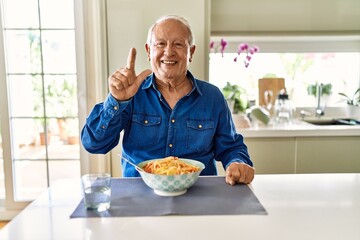 Wall Mural - Senior man with grey hair eating pasta spaghetti at home showing and pointing up with fingers number two while smiling confident and happy.