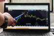 Working at the office, in front of the laptop. Online trading. Graphics on the laptop screen. Indicate the graph with a pen. Selective focus.