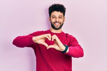 Poster - Young arab man with beard wearing casual pink sweater smiling in love showing heart symbol and shape with hands. romantic concept.