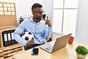 Wall Mural - Young african man football hooligan cheering game at the office pointing thumb up to the side smiling happy with open mouth