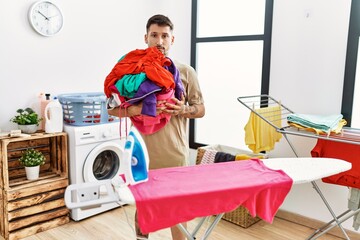 Poster - Young handsome man holding laundry ready to iron thinking attitude and sober expression looking self confident