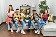 Group of young people watching football game wearing team scarf cheering game sitting on the sofa smiling happy pointing with hand and finger