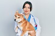 Beautiful hispanic veterinarian woman holding dog smiling looking to the side and staring away thinking.