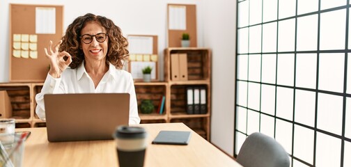 Canvas Print - Middle age hispanic woman working at the office wearing glasses smiling positive doing ok sign with hand and fingers. successful expression.