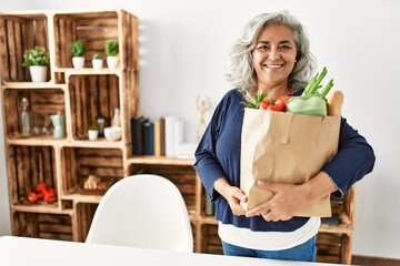 Canvas Print - Middle age grey-haired woman holding paper bag with groceries standing at home.